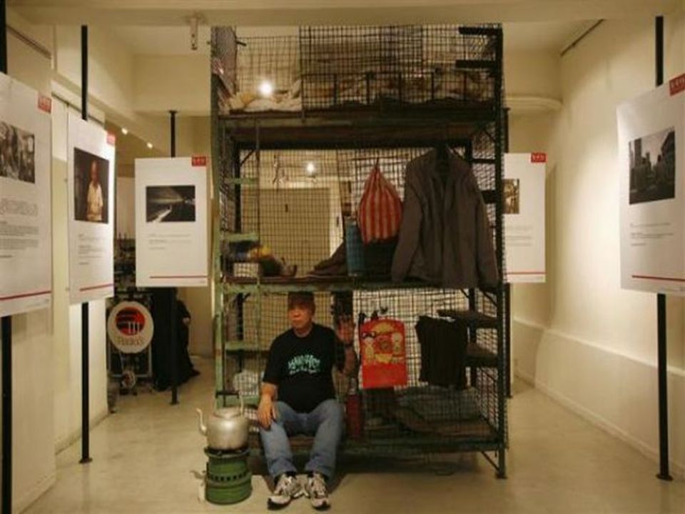 一位老人在堆满衣服和杂物的笼屋睡觉。 当主人离开房间时可将铁丝网封闭上锁防盗。